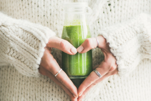 Woman holding wheatgrass juice to her stomach with heart