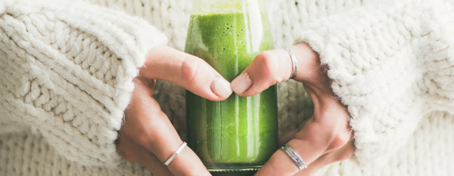 Woman holding wheatgrass juice to her stomach with heart