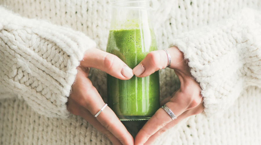 Woman holding wheatgrass juice to her stomach with heart